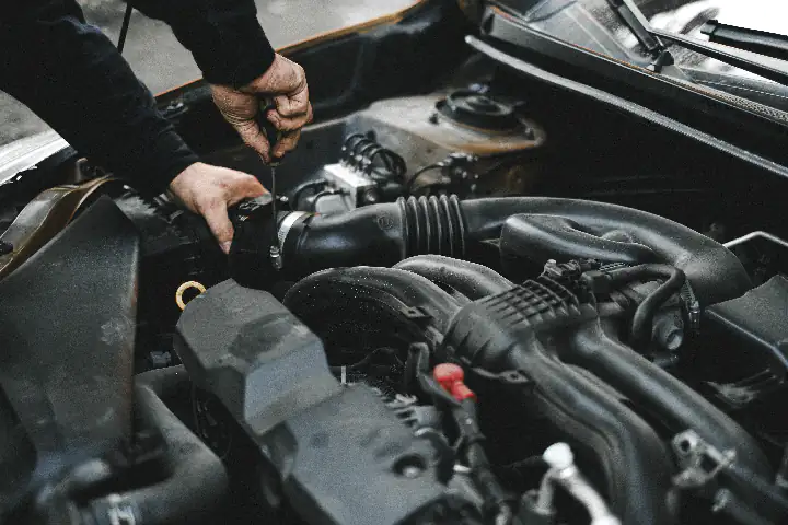 Dłonie mechanika samochodowego z narzędziem w jednej ręce przy silniku samochodu
